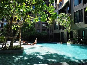 A pool area with clear water, surrounded by lush greenery and modern buildings. - The Base Central Phuket- 6 Floor (Wichit)