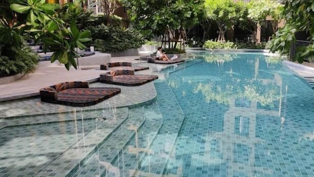 A swimming pool with tiled steps and lounge areas, surrounded by greenery. - The Base Central Phuket- 6 Floor (Wichit)