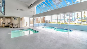 An indoor swimming pool with clear glass ceilings and windows, a lifeguard station, and a view of the cityscape. - Cozy 2BR/2BA Oceanfront Condo - Steps from the Beach! (Murrells Inlet)