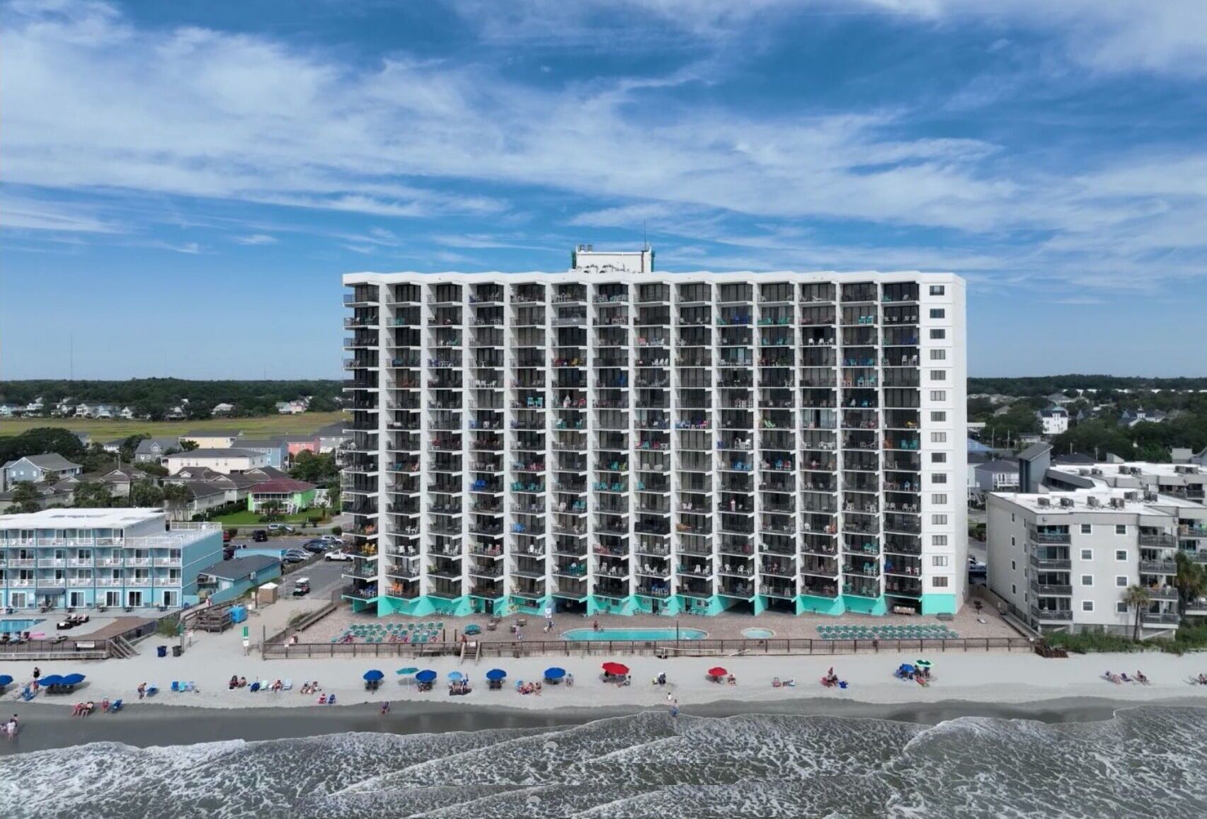 Een hoog hotel met meerdere balkons, een zwembad en voorzieningen aan het strand.