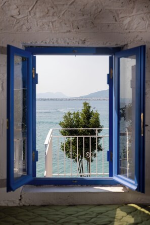 Enjoy a serene view from the room's open window, taking in the balcony with a tree and a distant body of water and mountains.