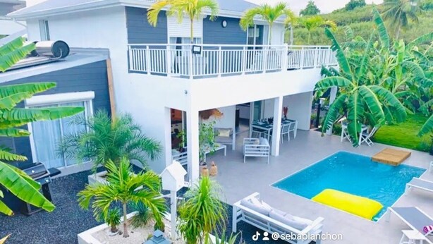 Una casa de dos pisos con balcón, piscina y plantas tropicales.