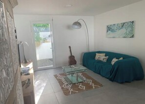 Una sala de estar con una mesa de centro de vidrio, un sofá color turquesa, una guitarra y un cuadro en la pared.