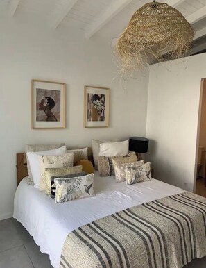 Un dormitorio con una cama grande, varios cojines, dos cuadros enmarcados y una lámpara colgante tejida.