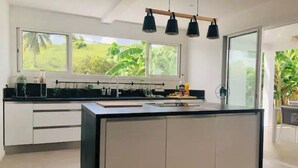 Cocina moderna con una isla grande, muebles blancos y vistas a exuberante vegetación.