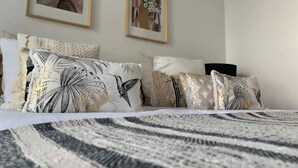 Una cama bien hecha con una colcha a rayas, una variedad de almohadas estampadas y dos cuadros en la pared.