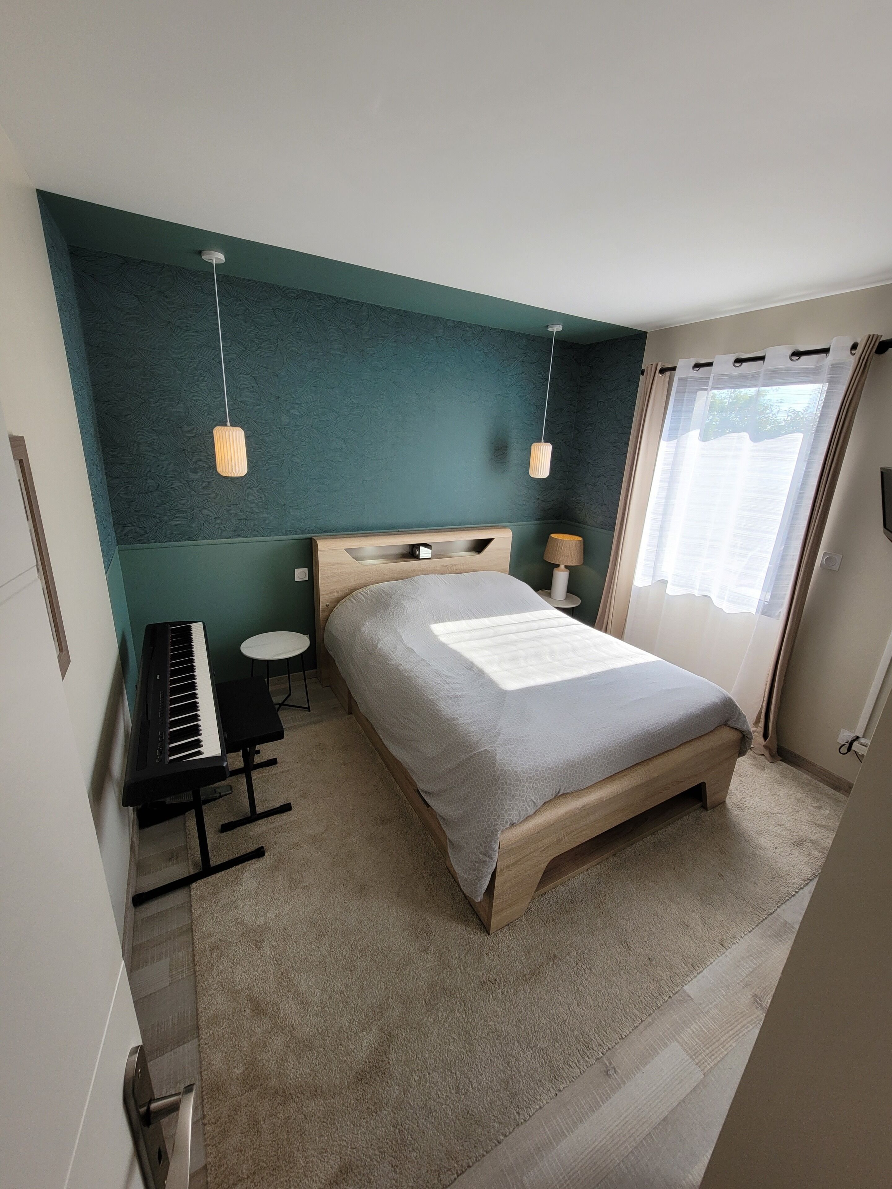 Een slaapkamer met een bed, een toetsenbord, een klein tafeltje en een wandlamp.