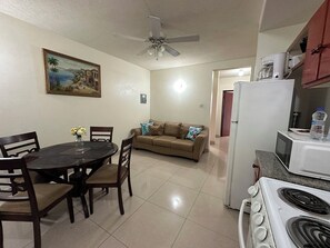 A kitchen with a stove, refrigerator, and microwave. There is a dining table with chairs and a couch in the background. - St. Lawrence Suites - Suite Five (Christ Church)