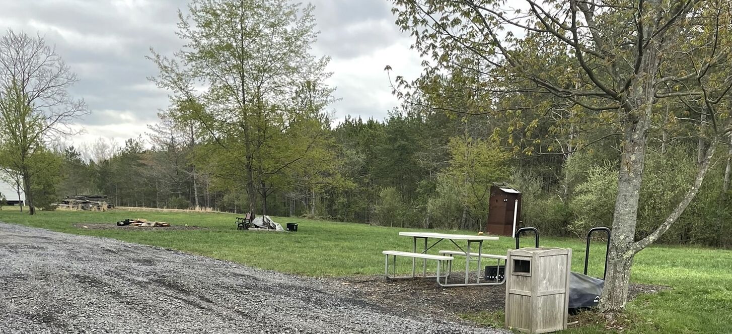 A campsite with picnic tables, a wooden shelter, and a gravel path.