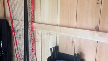 A wooden wall with a red and white netting structure, a black trash bin with tools, and a black bag on the floor.