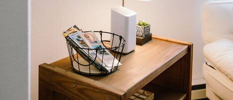 A wooden side table with a lamp, magazines, and a plant.