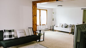 A living room with a black sofa, white sofa, and a coffee table. There is a window with curtains and a plant on the windowsill. - Come Visit “Mint To Be”
 (Somerset)