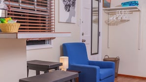 Ein Zimmer mit blauem Sessel, einem kleinen Tisch mit Lampe, einem Korbwäscheschrank und einer Wäscheleine.
