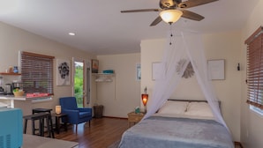 Ein Schlafzimmer mit einem Bett, einem Deckenventilator, einem Nachttisch mit Lampe, einem Stuhl und einem Schreibtisch mit Computer.