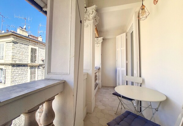 A narrow balcony with a stone balustrade, a white folding table, and a cushioned bench. - N&J - MADAGASCAR - Central - Very close sea (Niza)