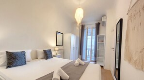 A bedroom with a large bed, two rolled towels, a bedside table with a lamp, a wardrobe, and a view of the outside through a glass door.