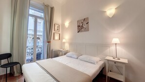 A hotel room with a bed, two bedside tables with lamps, a chair, a window with curtains, and artwork on the wall. - N&J - TERRACOTTA- Central - Proche mer (Niza)