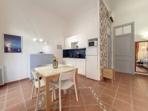 A compact kitchen with white cabinets, a microwave, and a small refrigerator. There is a dining table with chairs and a vase with flowers. The floor is tiled with a geometric pattern. - N&J - TERRACOTTA- Central - Proche mer (Niza)