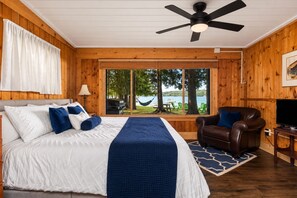 A bedroom with a bed, a leather chair, a television, and a view of the outdoors.