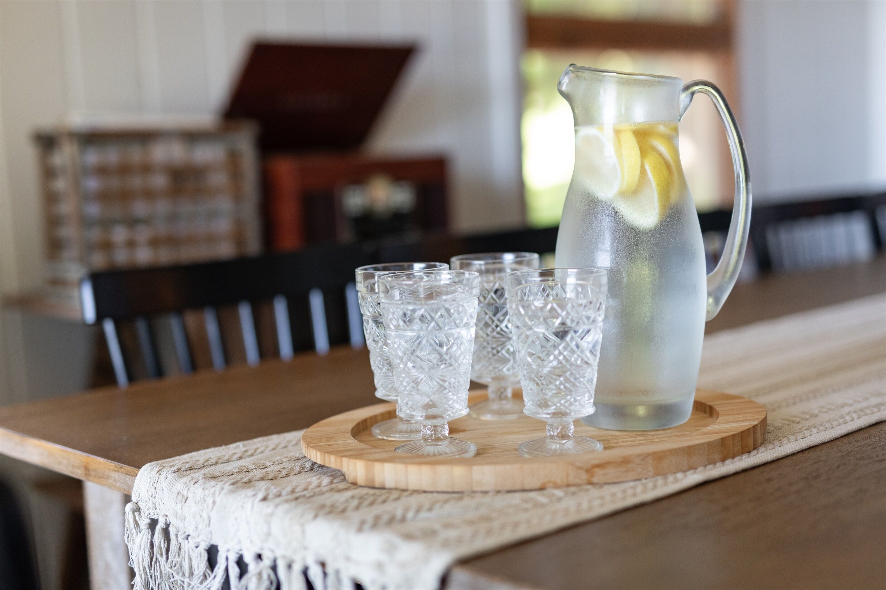 A wooden table with a pitcher and four glasses on a wooden coaster.
