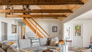 A cozy living room with a gray sofa, wooden coffee table, and a staircase. - Private Sandy Beach, Dock, Kayaks, Canoe & Paddleboat | Sleeps 12 | Dog Friendly (Central Lake)