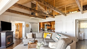 A spacious living room with a large sectional sofa, a fireplace, and a kitchen in the background. - Private Sandy Beach, Dock, Kayaks, Canoe & Paddleboat | Sleeps 12 | Dog Friendly (Central Lake)