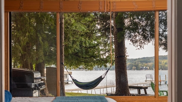 A bedroom with a bed, a hammock, and a view of a lake and dock. - Private Sandy Beach, Dock, Kayaks, Canoe & Paddleboat | Sleeps 12 | Dog Friendly (Central Lake)