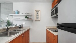 Una cucina moderna con mobili in legno, un lavello in acciaio inossidabile, un frigorifero nero e un forno a microonde. Sul piano di lavoro c'è una piccola pianta in vaso e un quadro appeso al muro.