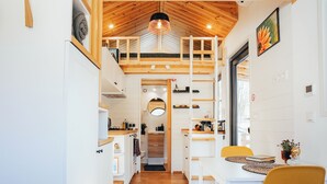 A modern kitchen with wooden beams, a dining area with yellow chairs, and a view into the living room. - Transylvanian Tiny House Apuseni Mountains. (Mătișești, Comuna Horea)