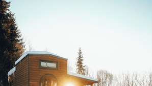 A wooden cabin with a circular window, surrounded by snow, and a wooden deck leading to it. - Transylvanian Tiny House Apuseni Mountains. (Mătișești, Comuna Horea)