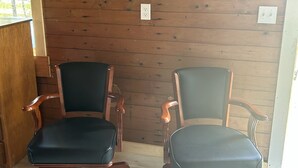 Kaksi pyörillä varustettua toimistotuolia, puinen seinä, jossa on kyltti, jossa lukee ”CAMP MUSKIE”, ja kehystetty kuva.