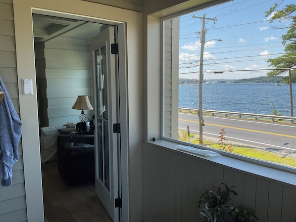 A room with a view of a lake, a window with a view of a road, and a door leading to another room.