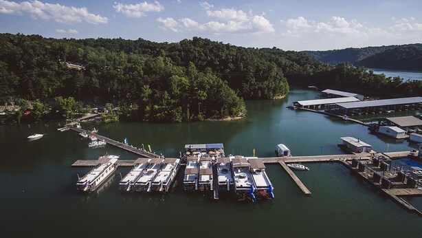 An aerial view of a marina with docked boats, a pier extending into the water, and a forested hillside in the background. - The Victorian @ Lake Cumberland - Beaver Creek, firepit, sleeps 18 (Monticello)