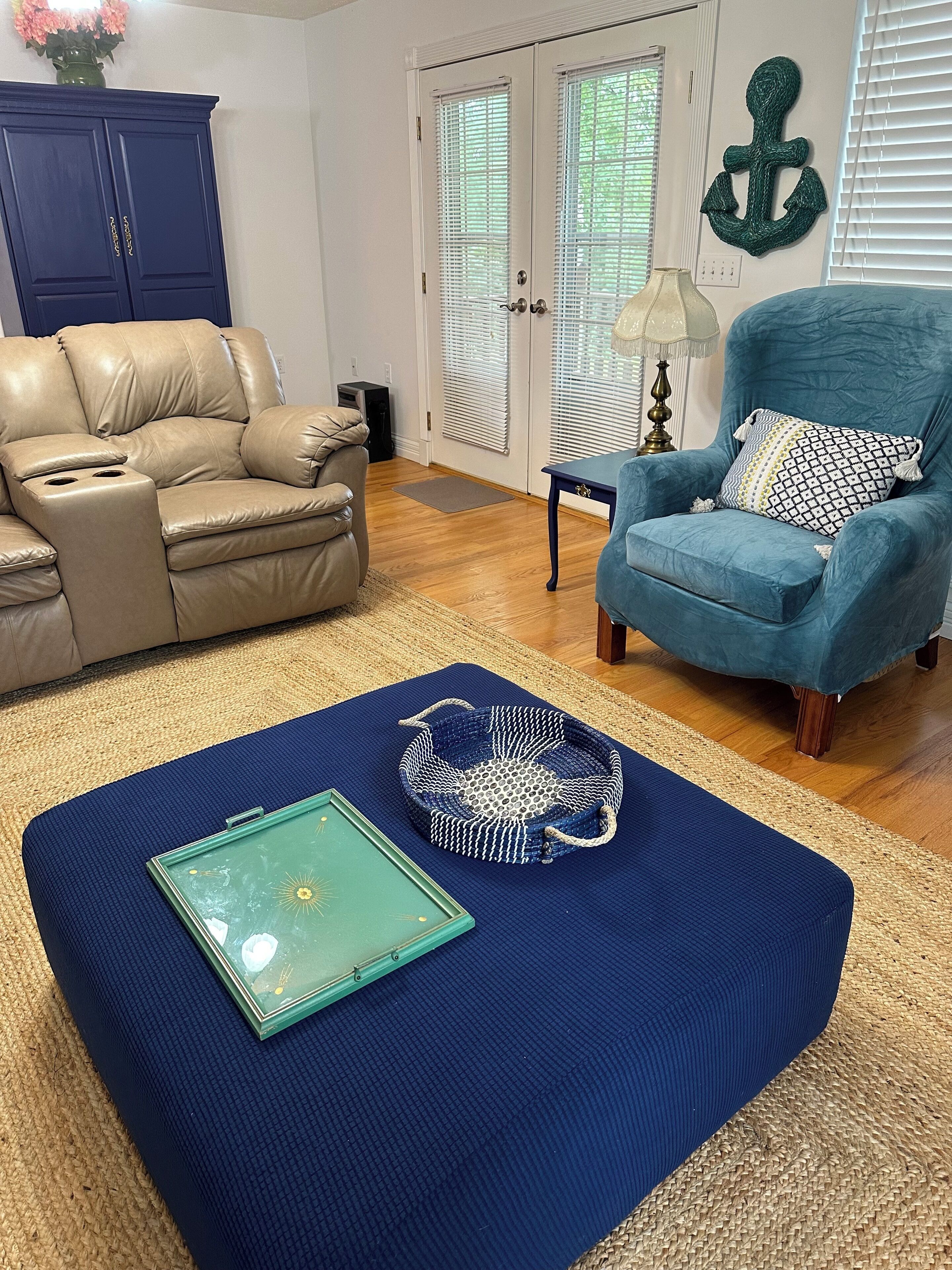 A living room with a beige leather sofa, a blue armchair, a blue rug, a green tray, and a woven basket.