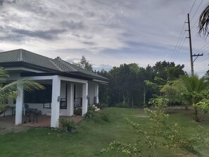 A single-story house with a covered porch, surrounded by a well-maintained lawn and various plants. - Home Harbor (Panglao)