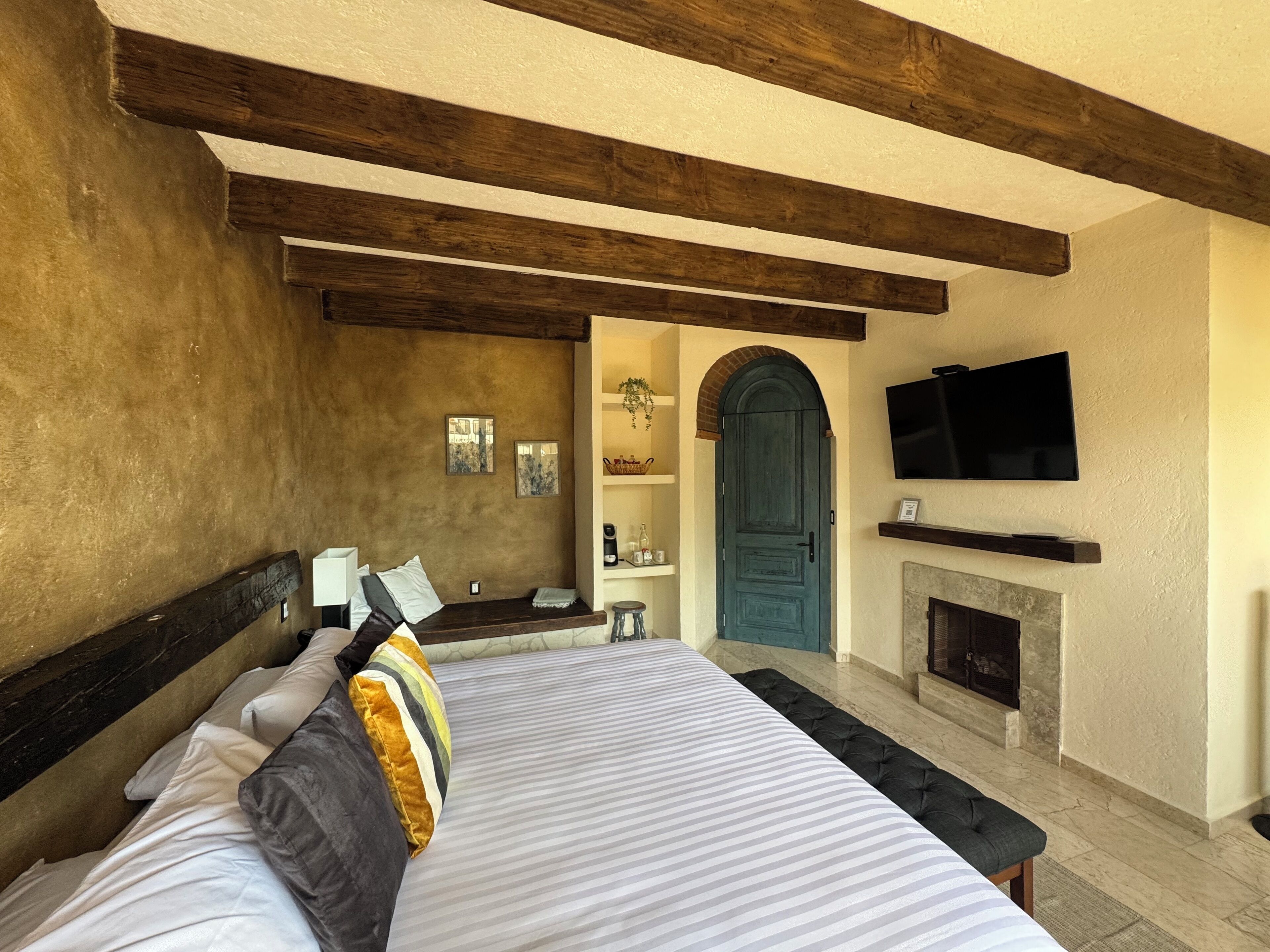 A bedroom with a bed, a bench, a TV, a fireplace, and a door.
