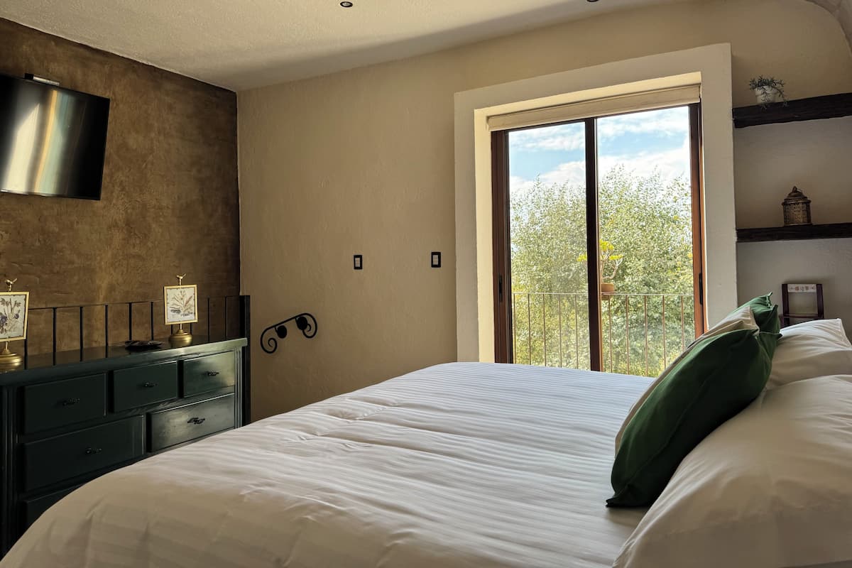 Un dormitorio con una cama grande, un aparador, un televisor de pantalla plana y una ventana con vistas a árboles.