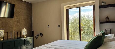 Una camera da letto con un letto grande, una cassettiera, una TV a schermo piatto e una finestra vista alberi.