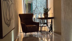 A hallway with a polished marble floor, a leather armchair, a table with candles, and a hanging plant.