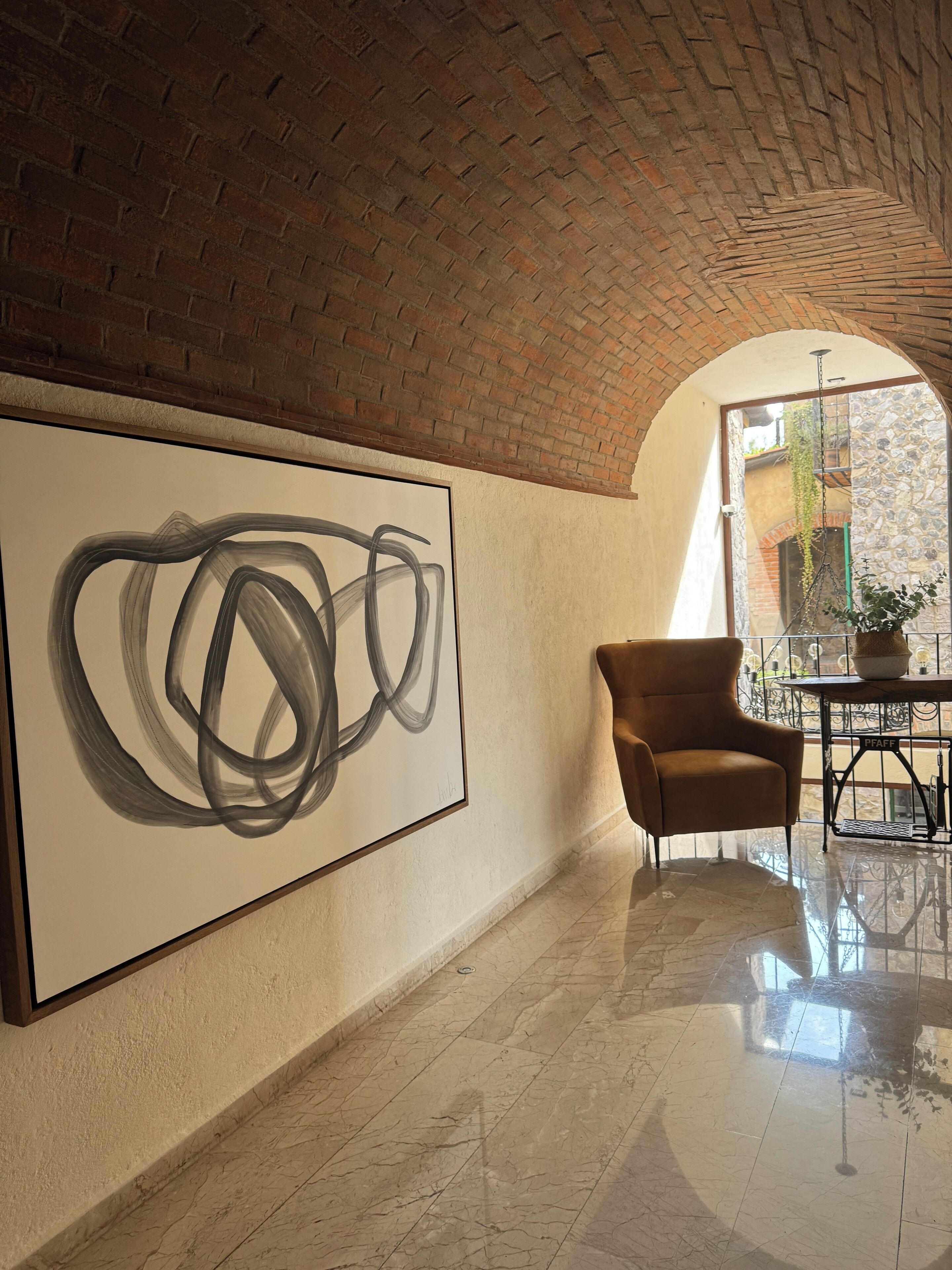 A spacious lobby with a large abstract painting, a brown armchair, and a stone wall.