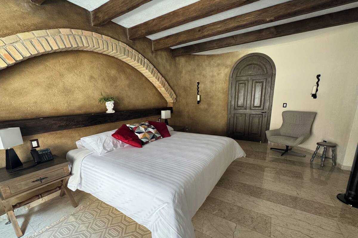 Un dormitorio con una cama grande, una mesita de noche de madera, un escritorio, una silla, una puerta y un arco en la pared.