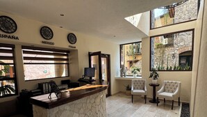 A reception area with a marble counter, a computer, and two chairs. There are clocks on the wall and a view of the outside through large windows.