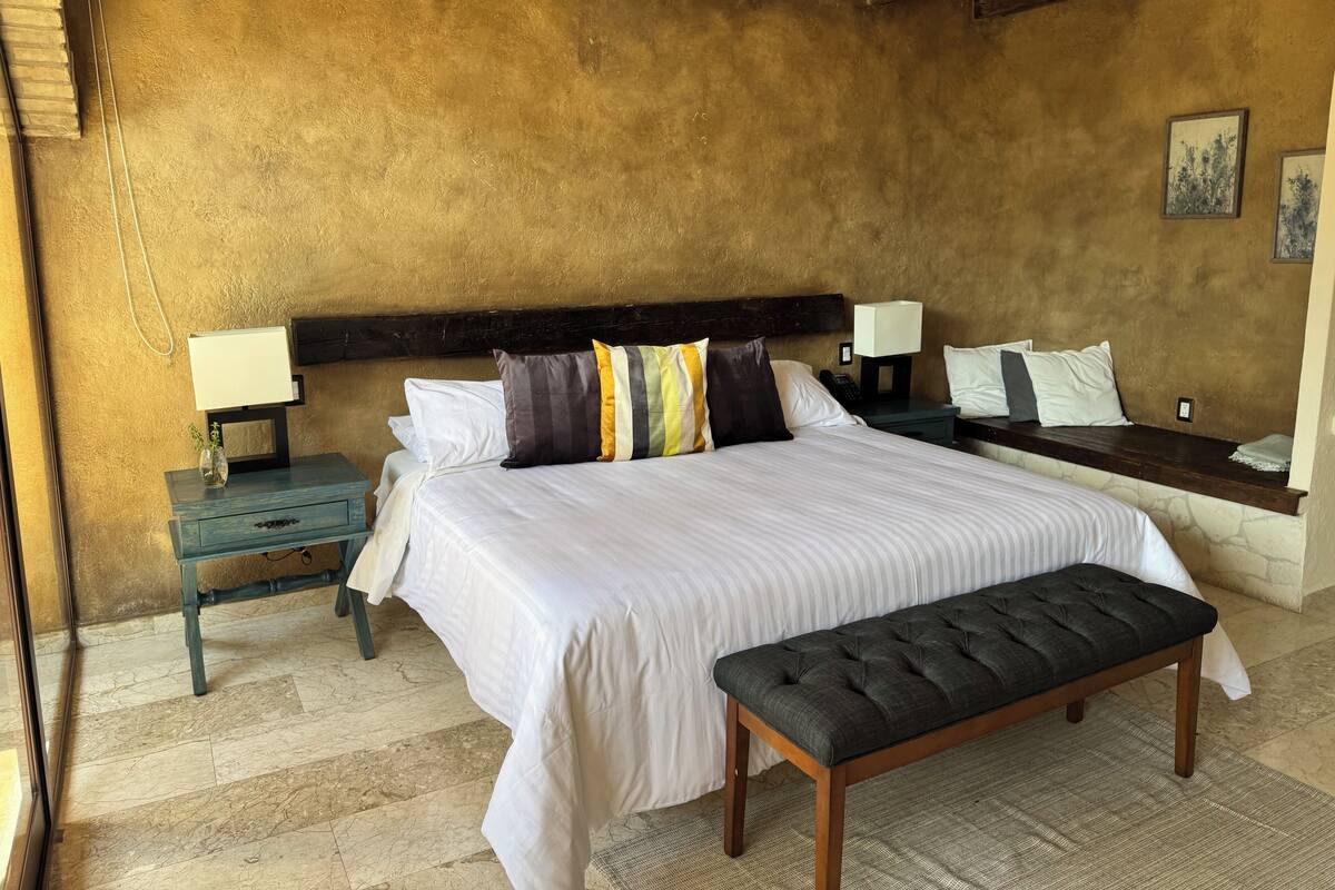Un dormitorio con una cama grande, dos mesitas de noche, un banco y una pared de piedra.