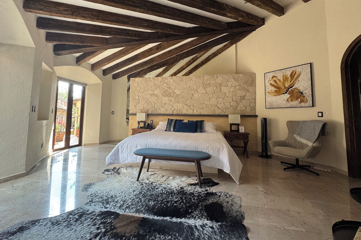 Un dormitorio espacioso con una cama grande, un muro de acento de piedra y una silla moderna.
