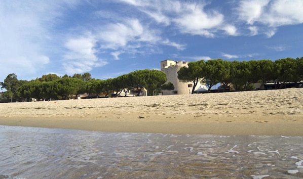 A beach with a sandy shore, a clear sky, and a building with a unique architectural structure.