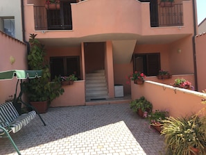 A building with a tiled patio, a staircase, and potted plants.