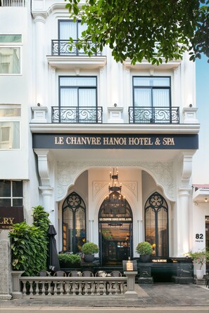 The facade of Le Chavre Hanoi Hotel & Spa, featuring a grand entrance with a black awning, potted plants, and a black signboard above the entrance. - Le Chanvre Hanoi Hotel & Spa (Hanoi)