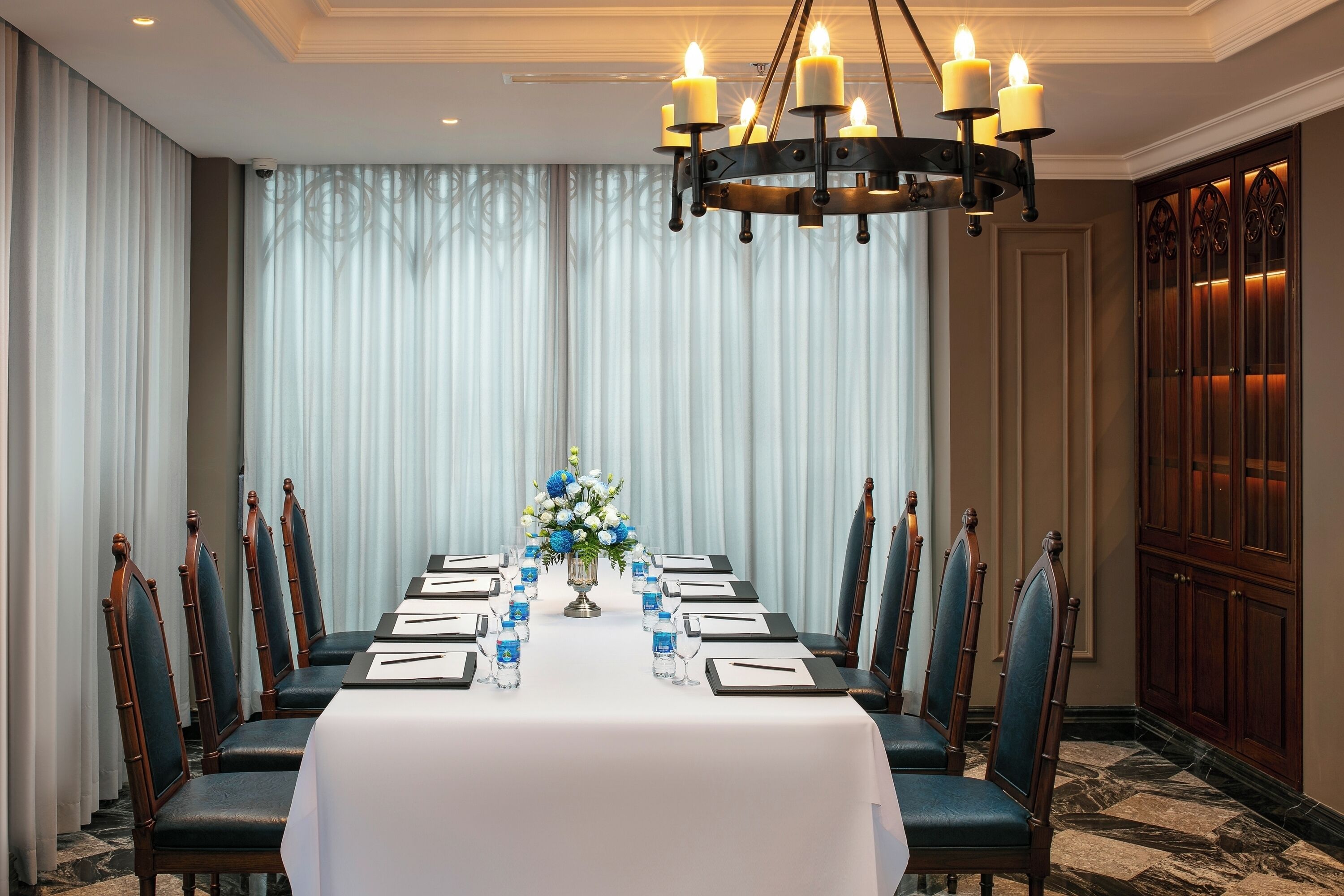 A conference room with a long table, chairs, a chandelier, and a floral centerpiece.