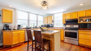 A modern kitchen with wooden cabinets, a central island with bar stools, stainless steel appliances, and large windows providing natural light. - 4BR Creekside Country Hideaway on 34 Acres - Pet Friendly (Middlebrook)