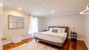 A bedroom with a large bed, a nightstand, a wall-mounted mirror, and a wooden floor. - 4BR Creekside Country Hideaway on 34 Acres - Pet Friendly (Middlebrook)